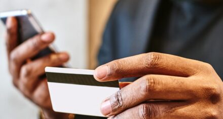 man holds phone and credit card while paying online